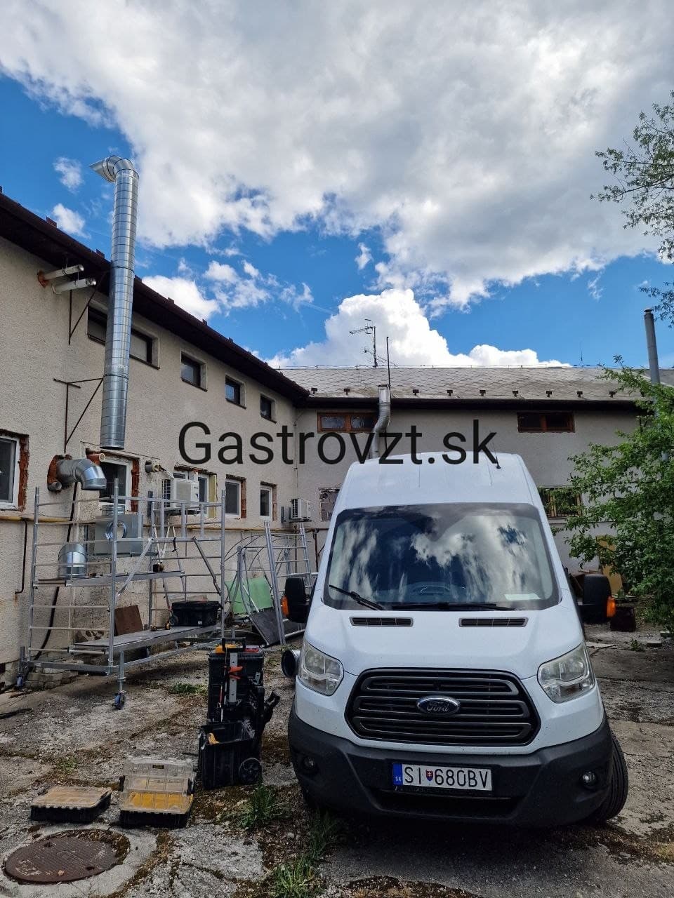 Firemné vozidlo Gastrovzt na objekte — lešenie, náradie a hotové potrubie na fasáde